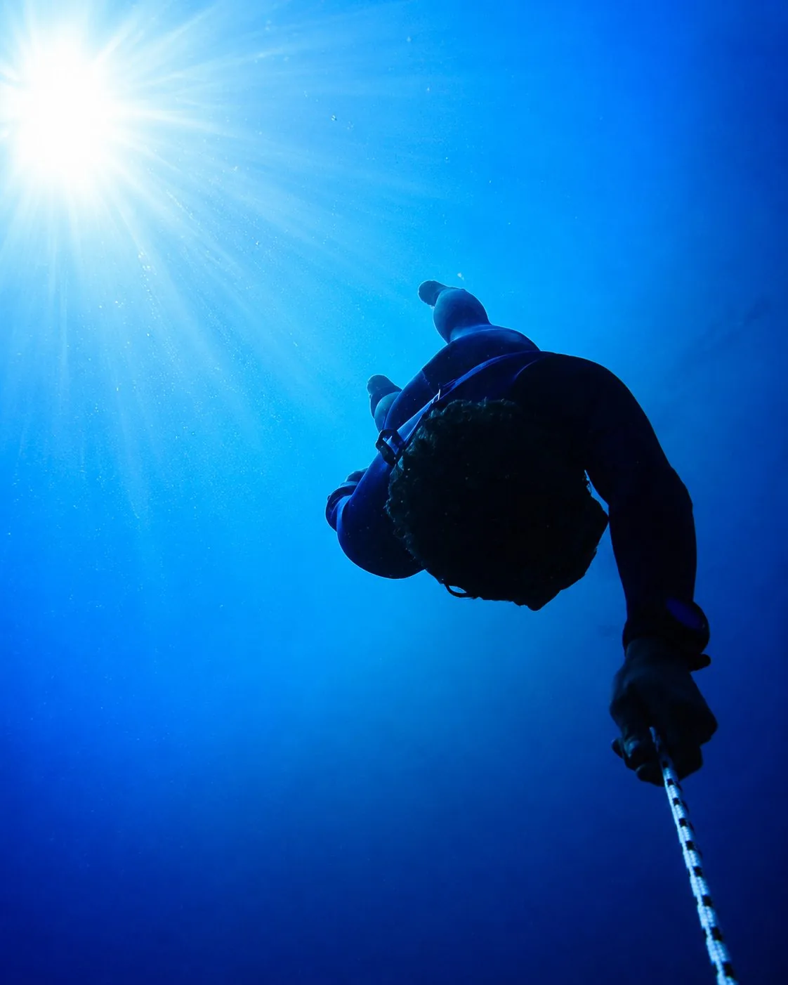 Apnéiste en pleine descente le long d'une ligne, silhouette face au soleil sous l'eau