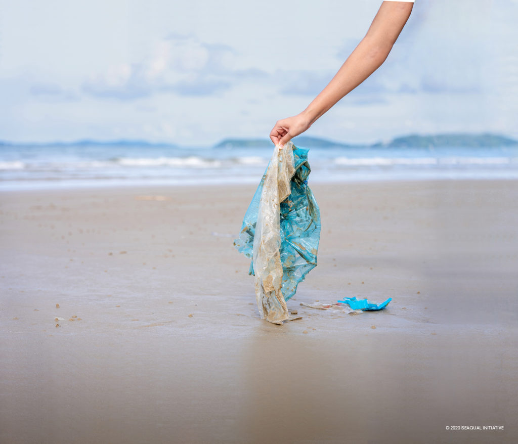 Woman’s hand picking up used plastic bag on sand beach, cleaning seaside beach.  Environmental pollution, Ecological problem and  Marine pollution concept.